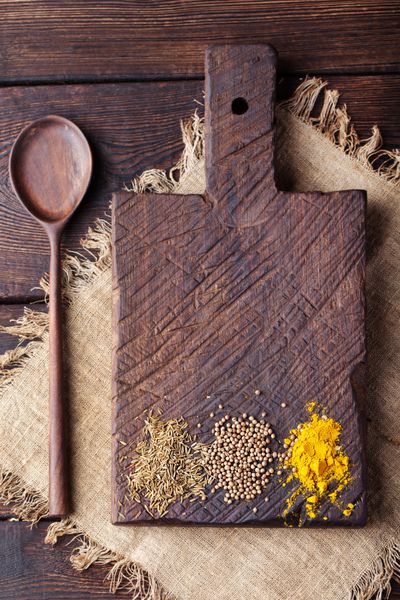 تخته برش چوبی و قاشق با ادویه جات زیره حمل زردچوبه دانه گشنیز روی یک میز چوبی قدیمی پس زمینه متن کپی sp