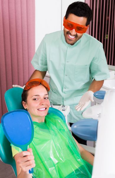 بیمار زن خوشحال که برای سفید کردن دندان به دندانپزشک مراجعه می کند