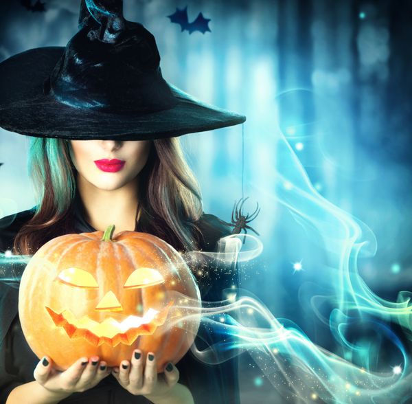جادوگر هالووین با کدو تنبل جادویی در یک جنگل تاریک زن جوان زیبا با کلاه و لباس جادوگر که کدو تنبل حک شده در دست دارد طراحی هنری هالووین