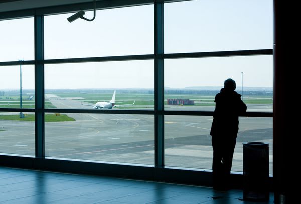 سالن فرودگاه یا محوطه انتظار با مرد تجاری که بیرون از پنجره ایستاده و به سمت برج کنترل نگاه می کند