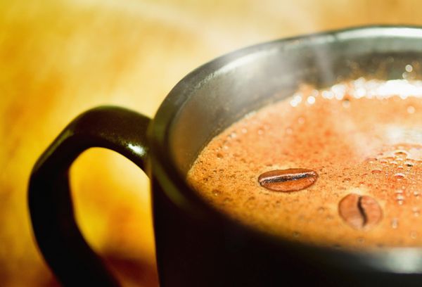 اسپرسو قهوه سیاه در یک فنجان با دانه های قهوه دانه های قهوه روی فوم برای طراحی شما نمای نزدیک از دو دانه قهوه در یک فنجان سیاه با بخار