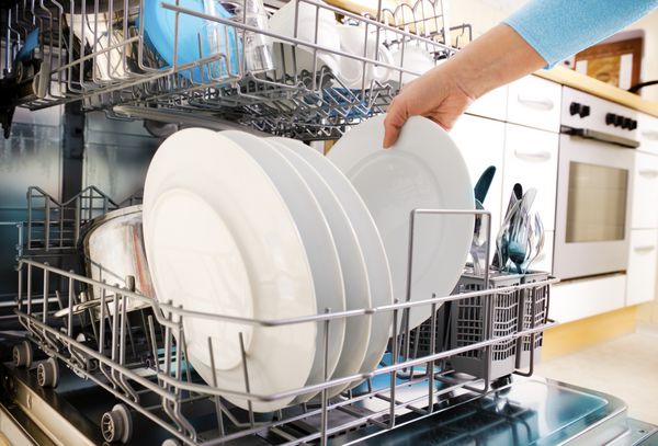 نمای نزدیک از دستان زن در حال بار کردن ظروف در ماشین ظرفشویی