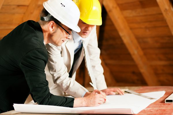 طرح ها و نقشه های بحث معمار و مهندس ساختمان یا نقشه بردار هر دو کلاه سختی به سر دارند و در محل ساخت و ساز یک خانه در داخل خانه ایستاده اند