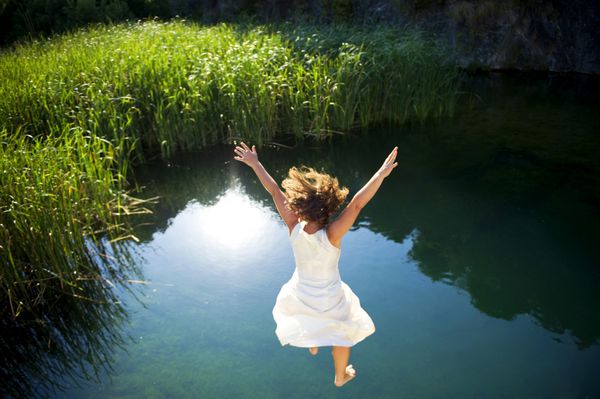 زن جوانی با لباس سفید در حال پریدن به دریاچه ای زیبا