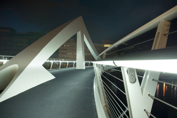 پل عابر پیاده مدرن بر روی رودخانه کلاید در گلاسکو اسکاتلند انگلستان اروپا از زاویه کم در شب برای نشان دادن نرده های روشن و اشکال هندسی