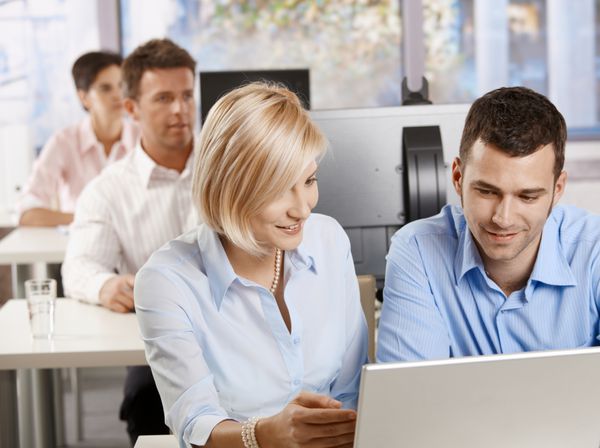 کسب و کار جوان پشت میز نشسته با استفاده از کامپیوتر در آموزش کسب و کار لبخند می زند