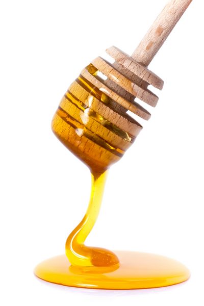 چکیدن عسل از دیپر چوبی عسل در پس زمینه سفید