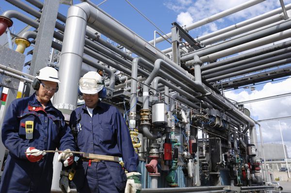مهندس نفت کارگران مقابل خط لوله بزرگ و ساخت سوخت در داخل پالایشگاه