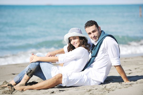 زوج جوان شاد با لباس سفید در تعطیلات در ساحل زیبا تفریح و سرگرمی عاشقانه دارند