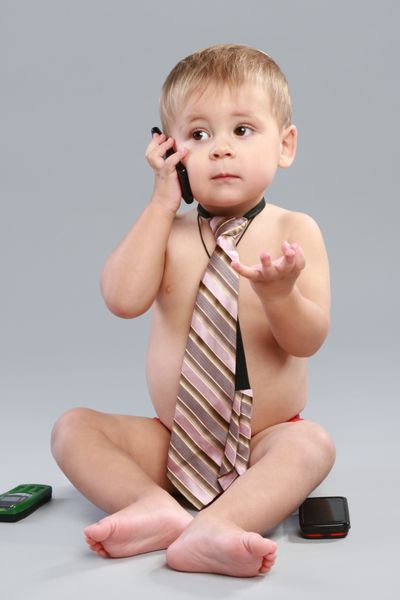 پسر کوچک کراوات با تلفن همراه در پس زمینه خاکستری صحبت می کند
