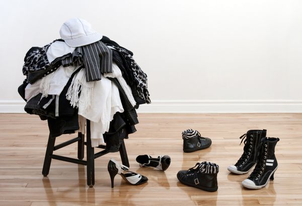 انبوهی از لباس‌های سیاه و سفید روی چهارپایه و کفش‌های نامرتب روی زمین چوبی
