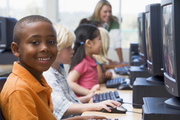 کودکان در پایانه های کامپیوتر با معلم در پس زمینه کلید عمق میدان بالا
