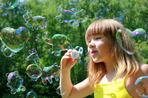 دختر بچه‌ای که حباب‌های صابونی به شکل حیوانات بامزه را باد می‌دهد