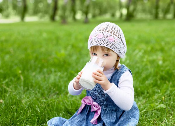پرتره یک دختر بچه شاد در حال نوشیدن شیر در پارک