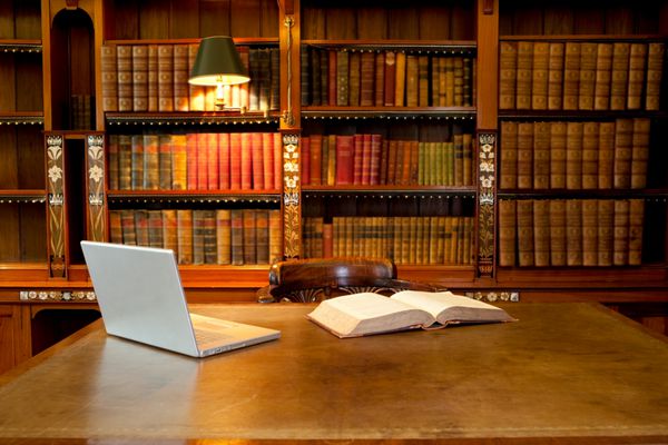 لپ تاپ و کتاب روی میز در کتابخانه کلاسیک خوابیده است