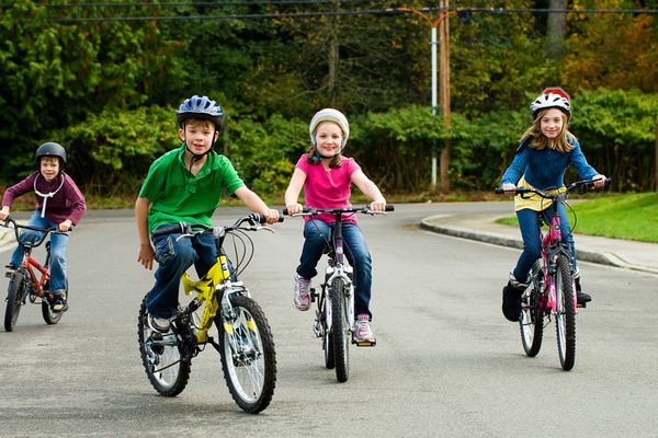 گروهی از کودکان شاد در حالی که کلاه ایمنی به سر دارند با خیال راحت در خیابان دوچرخه سواری می کنند