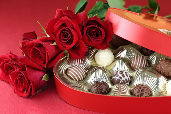نامزدی الماس در داخل یک جعبه ترافل شکلاتی به شکل قلب با گل رز قرمز فوکوس انتخابی روی حلقه الماس با پس زمینه تار نرم