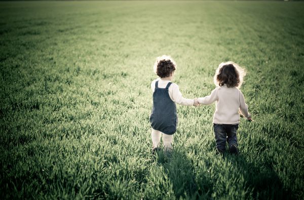 دو کودک که در زمین سبز بهاری می روند