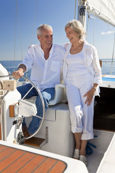 یک زن و شوهر سالمند شاد که روی یک قایق بادبانی روی دریای آبی آرام نشسته اند