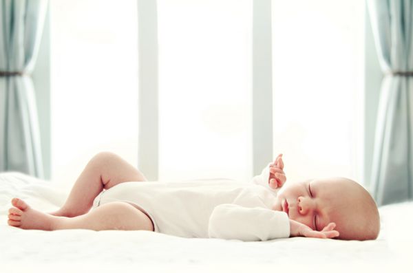 نوزاد تازه متولد شده روی پتوی سفید جلوی پنجره خوابیده است فوکوس نرم DOF بسیار کم عمق