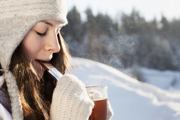 دختری جذاب در حال نوشیدن چای در پس زمینه طبیعت زمستانی در فضای باز