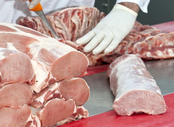 دست‌های قصابی که گوشت خوک را برای بازار گوشت تکه می‌کنند