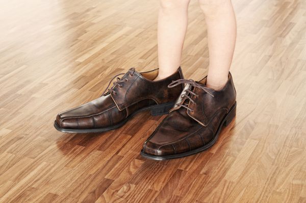 کفش های بزرگ برای پر کردن پای کودک در کفش های قهوه ای بزرگ روی کف پارکت گردویی