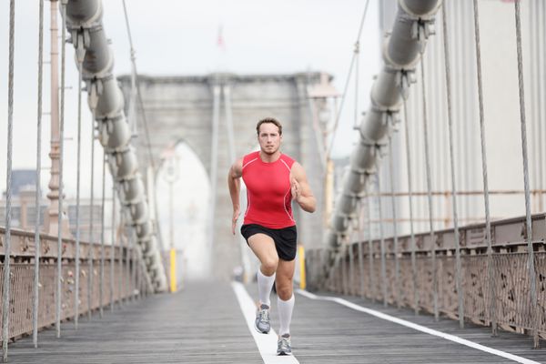 مرد دونده در حال دویدن با سرعت ورزشکار مرد در حال تمرین به تنهایی در تمام بدن با پوشیدن تاپ و جوراب قرمز رنگ در حین دویدن روی پل بروکلین شهر نیویورک ایالات متحده آمریکا