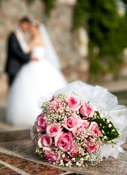 دسته گل رز روی پس زمینه داماد و عروس قرار دارد