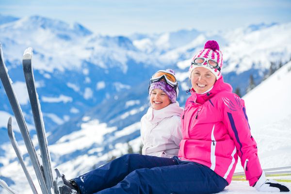 دختر جوان با مادرش لباس اسکی که در زمستان در فضای باز در تیرول اتریش روی برف می پرد