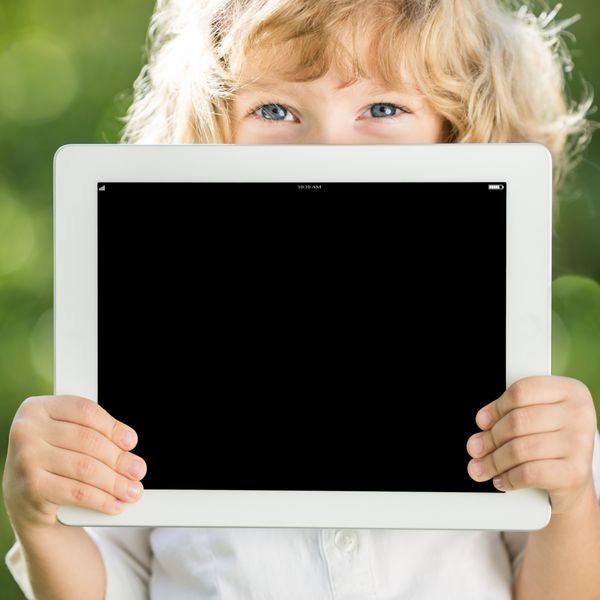 کودک شاد که تبلت رایانه شخصی را در فضای باز در پارک بهار نگه می دارد