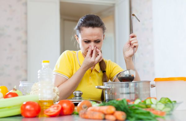 زنی که بینی خود را به دلیل بوی بد سوپ در تابه آشپزخانه گرفته است