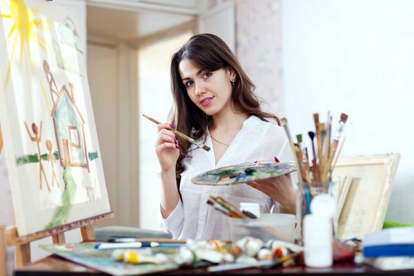 زن جوان در کارگاه خانه رویاها را روی بوم نقاشی می کند