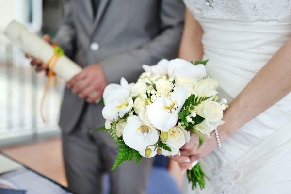دسته گل عروسی در دستان عروس در پس زمینه داماد با قرارداد عروسی