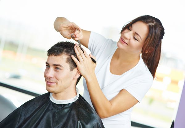 آرایشگر زن که موهای مشتری مرد خندان را کوتاه می کند