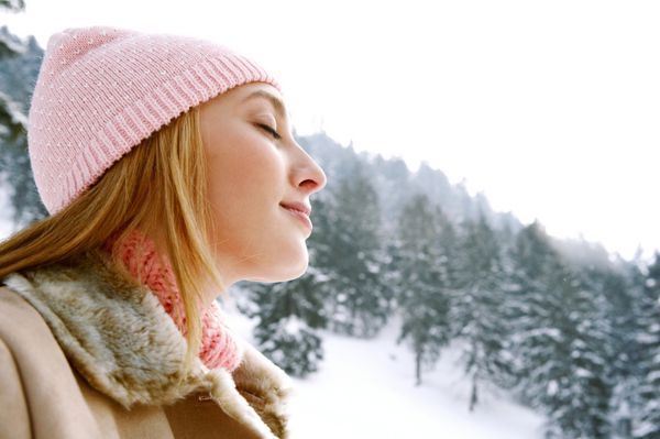 پرتره زیبایی جانبی نزدیک از یک زن جوان و جذاب که هوای تازه را در کوهستان های برفی با چشمان بسته تنفس می کند و در یک روز سرد زمستانی در فضای باز احساس سلامت و رویایی می کند