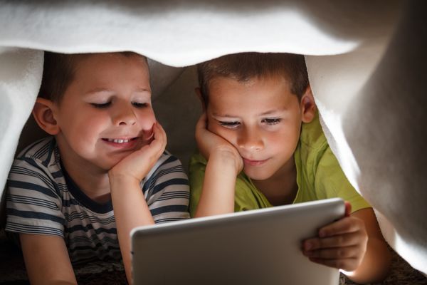 دو کودک که تبلت دیجیتالی را زیر پتو نگه داشته اند