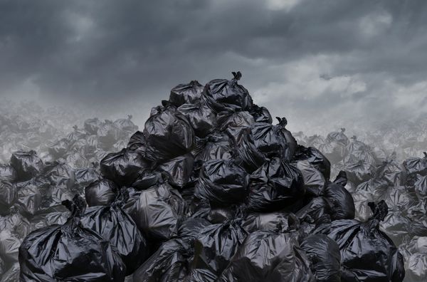 مفهوم زباله گاراژ به عنوان کوه‌هایی از کیسه‌های زباله سیاه با بوی نامطبوع در منظره‌ای بی‌نهایت توده زباله به عنوان پس‌زمینه مسائل آسیب‌های زیست‌محیطی در یک صحنه ابری تاریک مه‌آلود