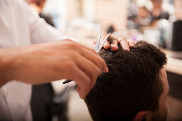 نمای نزدیک از مرد جوانی که در یک مغازه گیلاس موهایش را کوتاه می کند