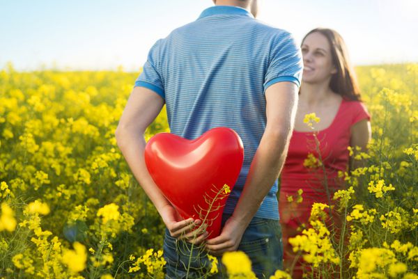 زوج جوان شاد عاشق بادکنک قلبی شکل در مزرعه کلزای زرد