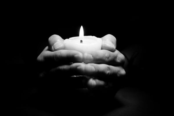 دست های دعا با شمع در پس زمینه تیره سیاه و سفید
