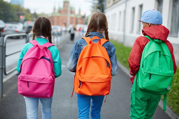 پشت بچه های مدرسه ای با کوله های رنگارنگ در حال حرکت در خیابان