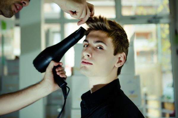 مرد جوان در سالن زیبایی از آرایشگاه برای کوتاه کردن موی مرد جوان استفاده می کند مدل مرد مد پشت صحنه