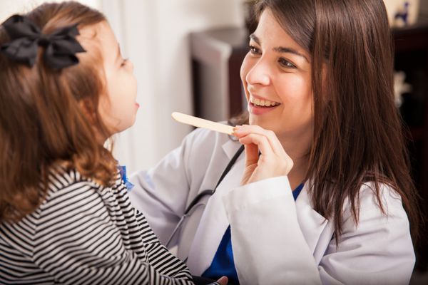 پرتره یک متخصص اطفال جوان زیبا که دهان یک دختر بچه را در یک کلینیک معاینه می کند