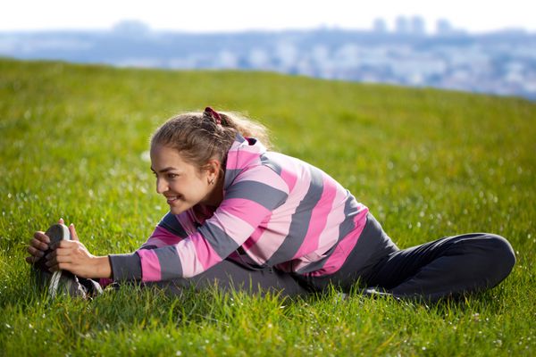 زن جوان زیبا در حال انجام تمرینات روی چمن در پارک شهر