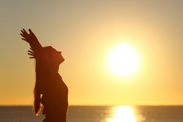 زنی که هنگام غروب آفتاب در ساحل هوای تازه نفس می کشد و بازوها را بالا می برد