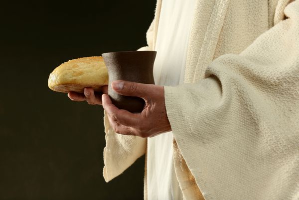 عیسی نان و یک فنجان جدا شده در پس زمینه تیره در دست دارد
