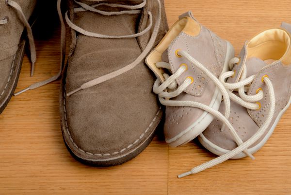 نمای نزدیک از کفش های پدری نزدیک به کفش های کودک در کف پارکت