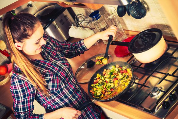 زن در آشپزخانه در حال آشپزی سبزیجات یخ زده سرخ کرده دختر در حال سرخ کردن و درست کردن غذای شام خوشمزه اینستاگرام فیلتر شد