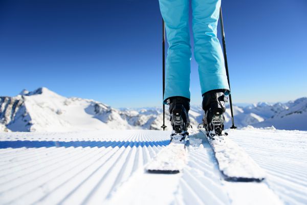 دختر اسکی روی برف تازه روی پیست اسکی تازه آراسته در روز آفتابی در کوهستان ایستاده است